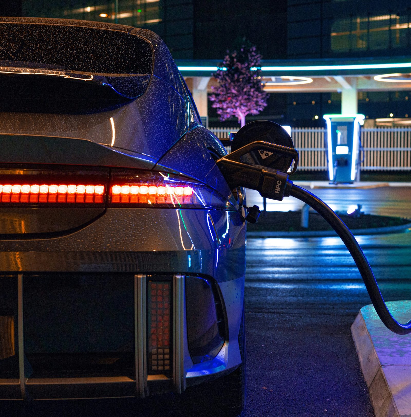 Electric car connected to a high-power DC fast charger on a rainy night